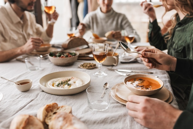 Close up group of young people sitting at the table full of delicious food having lunch in cozy cafe