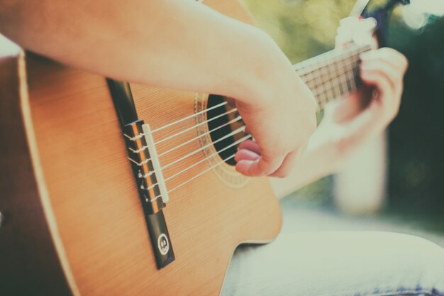 Primo piano del collo della chitarra con capo nel parco giovane uomo seduto sulla panchina che suona la chitarra