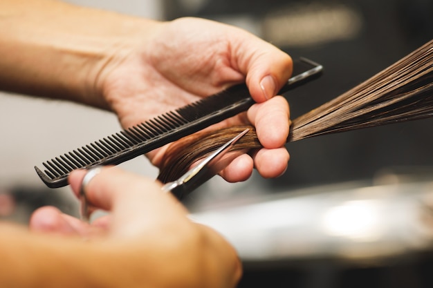 Close-up of hairdresser male hands during cutting female hair