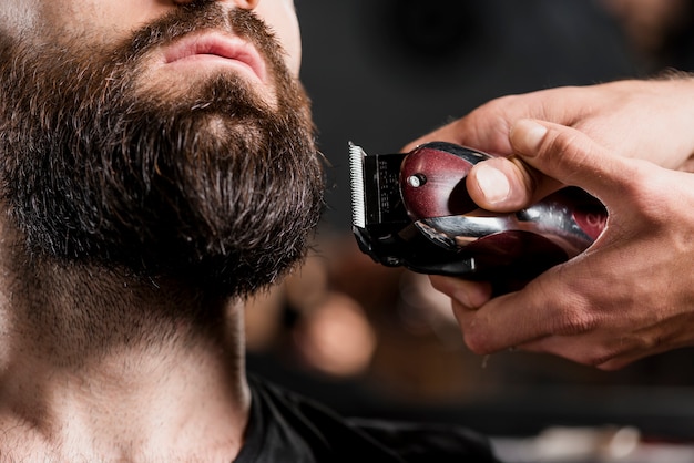 Photo close-up of a hairdresser's hand shaving man's beard with electric trimmer