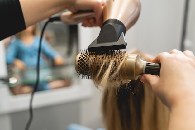 Close up of hairdresser that blowing dry while doing hair styling, urban beauty salon. Beauty concept