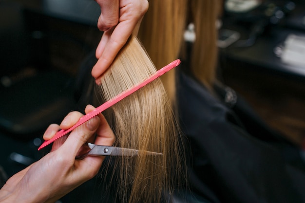 Photo close-up of hairstylist hands combing blonde hair before haircut in salon