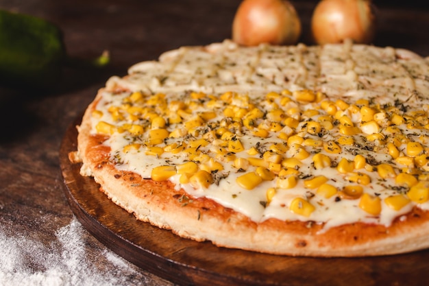 Close-up of a half corn half mozzarella cheese pizza on a wooden table.