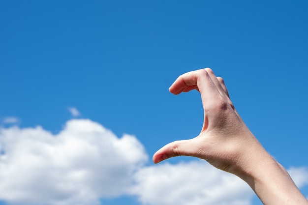 Close-up of half heart shaped hand gesture against clouds and blue sky. The concept of loneliness, love. Copy space.