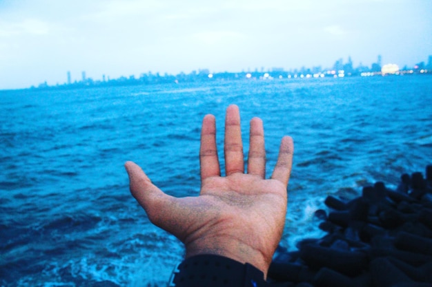 Close-up of hand against blue sea