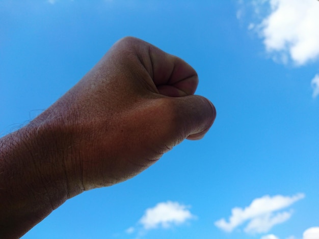 Close-up of hand against blue sky