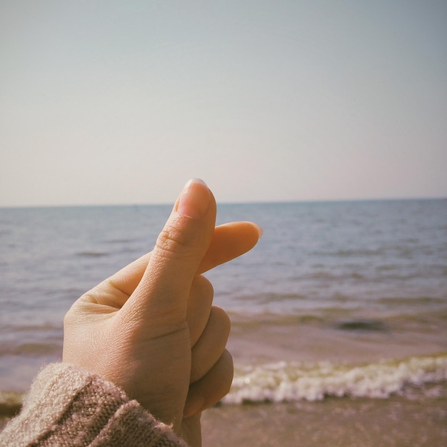 Close-up of hand against sea against sky