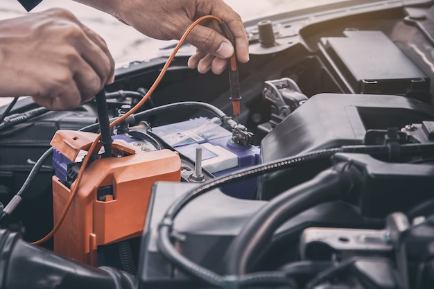 Close-up hand auto mechanic using measuring equipment tool for checking car battery.