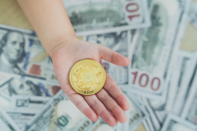 Close up of hand baby holding gold bitcoin crypto currency blockchain on dollar bill background on table Crypto currency blockchain Saving investment wealth concept