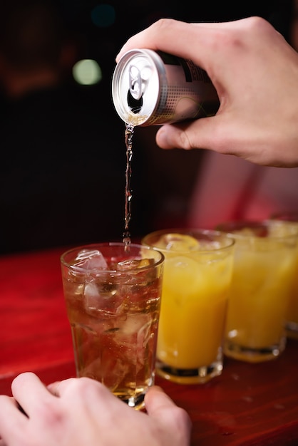 Close-up hand of bartender pours energy drink into alcoholic cocktail with orange juice in nightclub