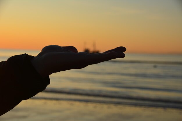 Foto close-up di una mano sulla spiaggia contro il cielo durante il tramonto