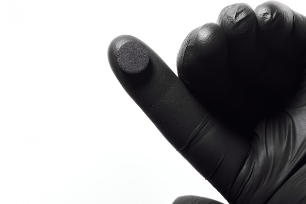 Close-up of hand in black latex glove holding black pill.