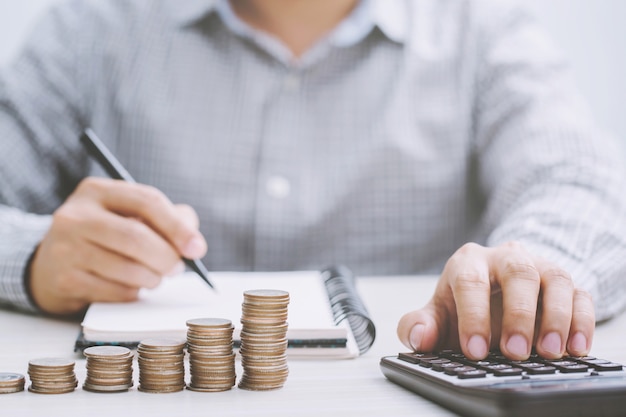 Close up hand business man accounting with savings money coins stacked row with hand putting coins in jug glass