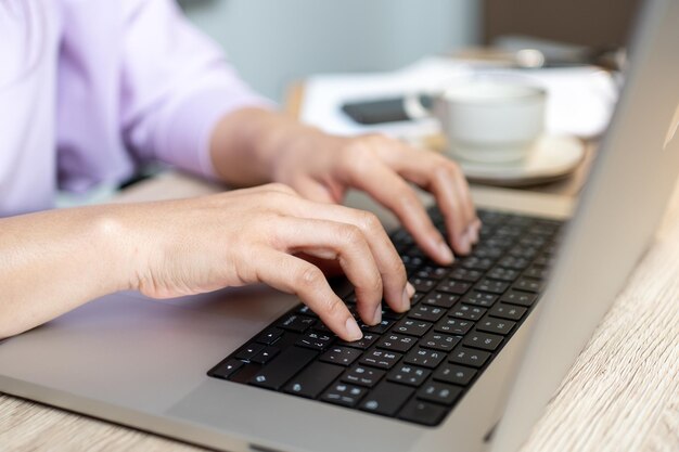 Chiuda sulla mano di una donna d'affari digitando il computer portatile della tastiera sulla scrivania dell'ufficio