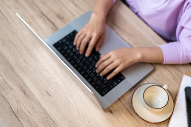 Chiuda sulla mano di una donna d'affari digitando il computer portatile della tastiera sulla scrivania dell'ufficio