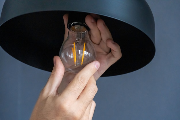 Close-up. A hand changes a light bulb in a stylish loft lamp. Spiral filament lamp. Modern interior decor.