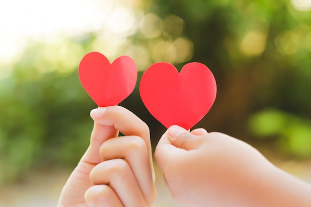 Close up hand of children holding mini heart on green background. 