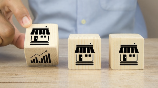 Close-up hand choose graph icon on cube wooden toy blocks place in line up with franchise business store icon.