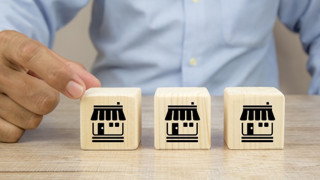 Close-up hand chooses cube wooden toy blocks stacked with franchise business store icon.