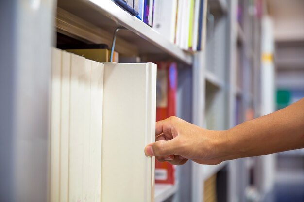 Close up hand choosing a book from bookshelf.