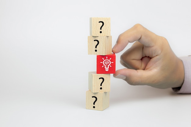 Close up hand choosing a light bulb icon from question mark symbol on cube wooden toy blocks