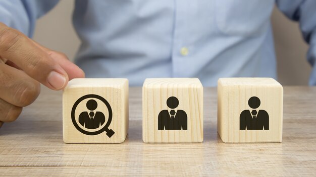 Close up hand choosing people in a magnifying glass icon on cube wooden toy blocks