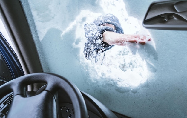 Photo close-up of hand cleaning snow on car windshield seen through glass