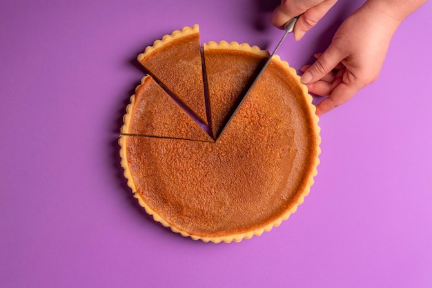 Close-up of hand cutting pastry on purple background