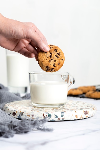 Photo close-up hand dipping chocolate cookie in milk