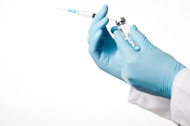 Close up hand of doctor in blue latex glove with glass ampoule and syringe on white background