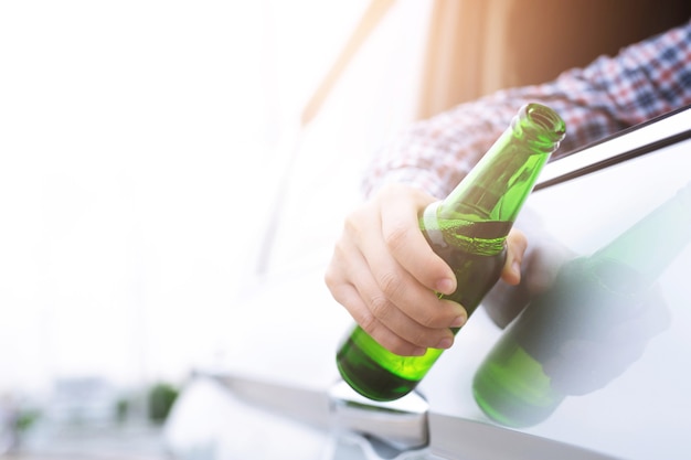 Close-up hand Dronken jonge man tijdens het besturen van een auto met een flesje bier.