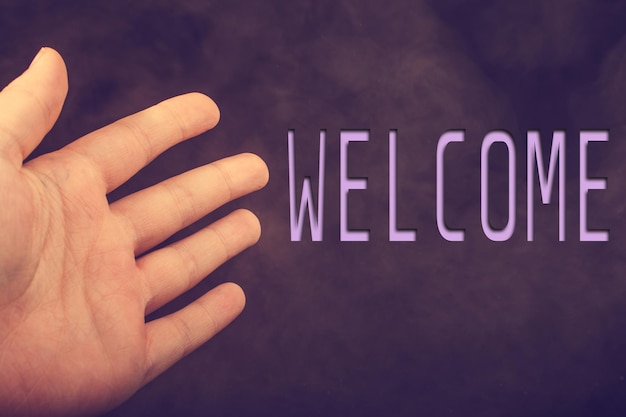 Close-up of hand gesturing at welcome text on purple wall