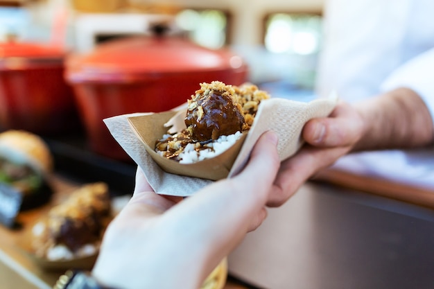 Close-up of the hand of a girl picking up the meatballs she has bought in a food truck.