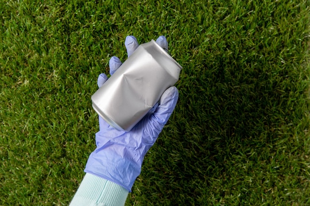 close up of hand in glove with used can on grass