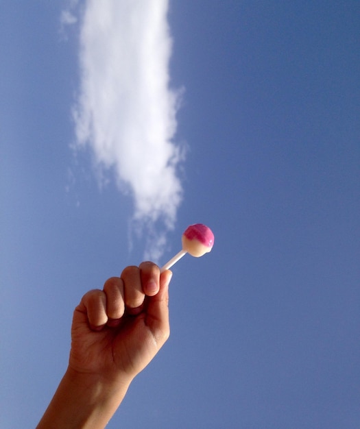 Close-up of hand holding balloons against blue sky