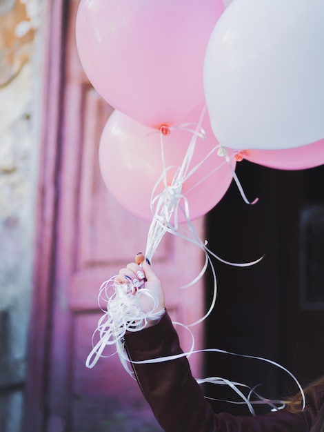 Photo close-up of hand holding balloons against pink door