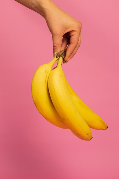 close-up of hand holding bananas against pink background