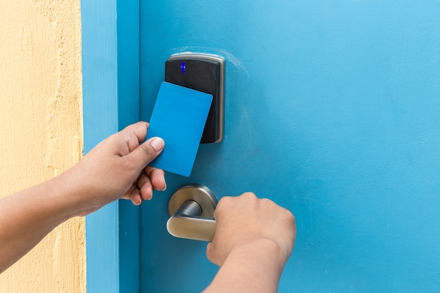 Close up hand holding blue hotel keycard in front of electric door