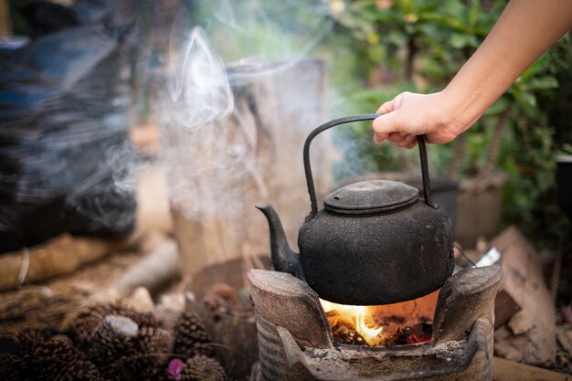 Close up hand holding boil water old kettle on the fire with a charcoal stove at blurred background