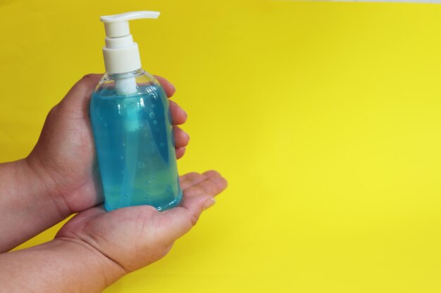 Close-up of hand holding bottle against yellow background