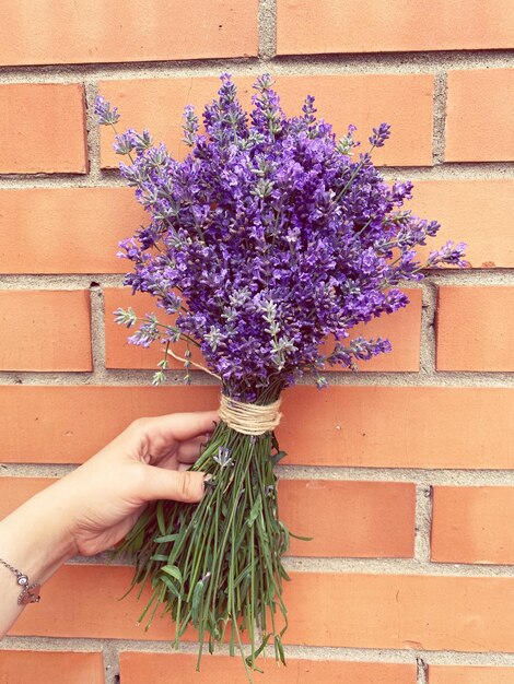 Foto close-up di una mano che tiene un bouquet contro il muro