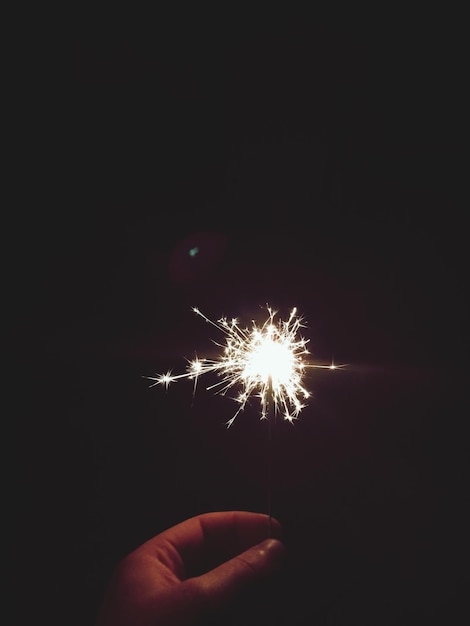 Foto close-up di una mano che tiene una scintilla accesa di notte