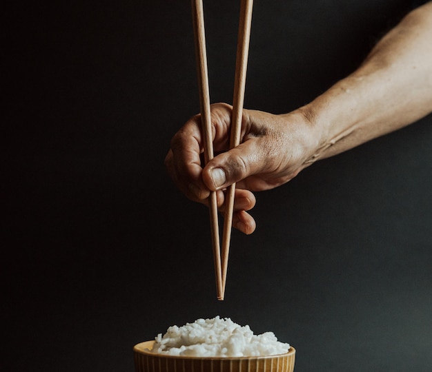 黒い背景にチョップスティックを握っている手のクローズアップ