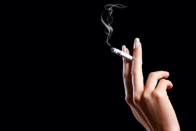 Photo close-up of hand holding cigarette against black background