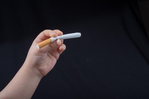 Close-up of hand holding cigarette over black background