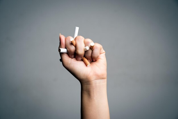 Close-up of hand holding cigarettes against gray background