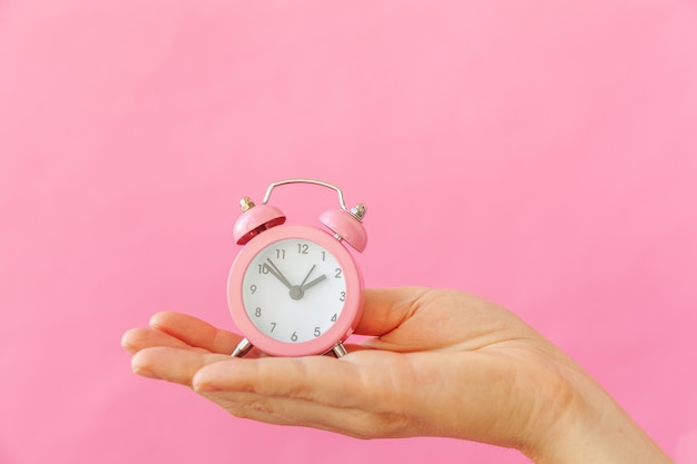 Close-up of hand holding clock against pink background