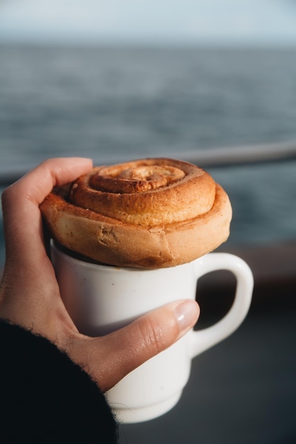 Foto close-up della mano che tiene il caffè e il panino alla cannella
