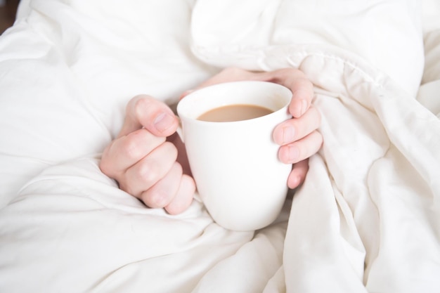 close-up of hand holding coffee cup on bed at home