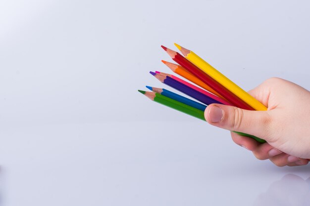 Close-up of hand holding colored pencils against white background